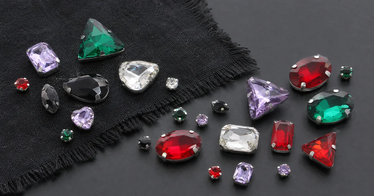 Piezas de pedrería de vidrio multicolor con engastes metálicos visibles junto a una muestra de tela oscura