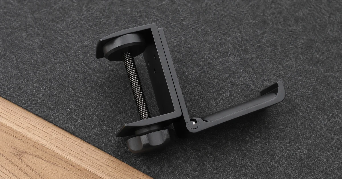Soporte negro para auriculares con pinza, sobre una alfombrilla de escritorio antes de instalarlo